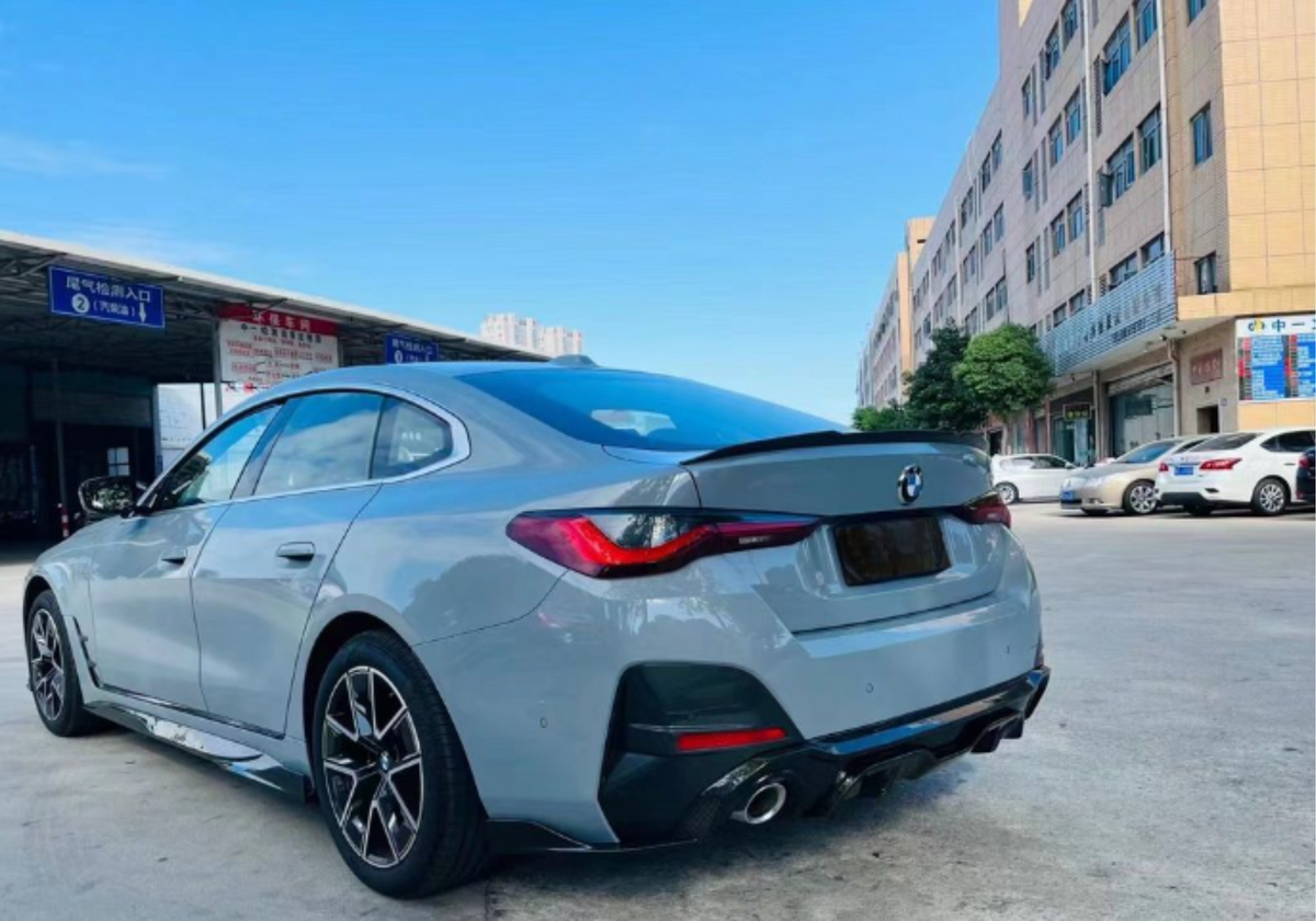 A gray car is parked near a commercial building under a clear sky. Nearby, other vehicles and signs with Chinese text are visible, indicating a bustling urban environment.
