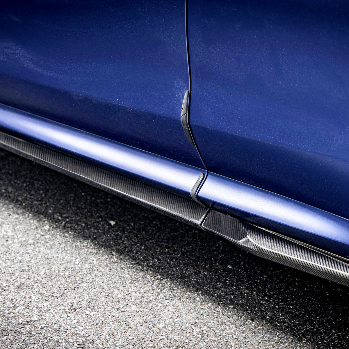 A blue car with side skirts and a visible tire on an asphalt road. The text "SPORTCONTACT" and "SODRUD" are marked on the components.