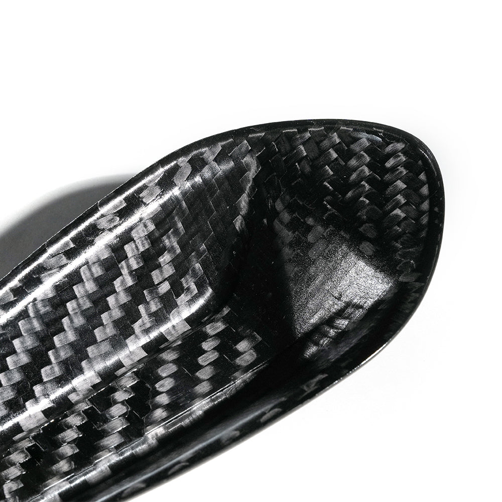 A close-up of a carbon fiber object, possibly a part of sports equipment, displaying a woven pattern. It is set against a plain white background.