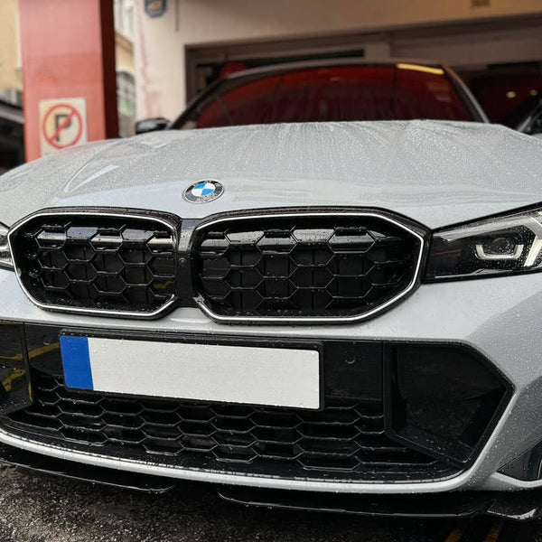 A silver BMW car parked in a garage, its hood covered in raindrops. A no-parking sign is visible on a red post nearby.
