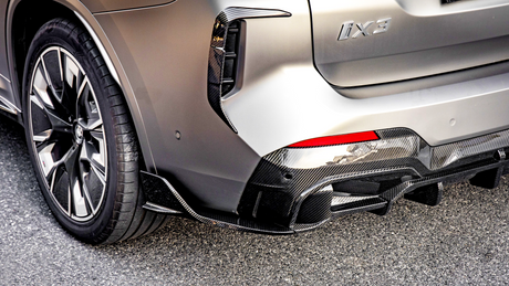 A car's rear section with a silver body and carbon fiber trim showcases a sleek tire design and red taillight. The badge reads "iX3." It's parked on asphalt.