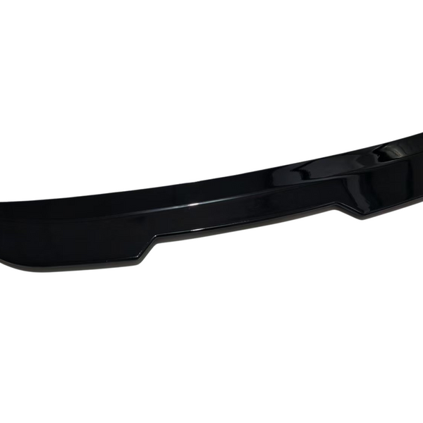 A black car spoiler with a sleek, curved design rests on a plain white background, highlighting its glossy finish and aerodynamic shape.