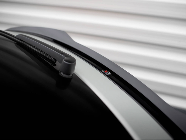A car's rear windshield features a wiper at rest, with a subtle "D" logo on the opposite edge. The vehicle is parked against a corrugated, white metal backdrop.