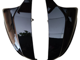 Two glossy black side mirrors are positioned facing each other against a white background, reflecting faint indoor patterns and light.