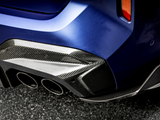A car's blue rear bumper features a glossy carbon fiber diffuser with three exhaust pipes, parked on an asphalt surface. The setting suggests a modern automotive design.