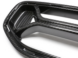 A carbon fiber car grille with a glossy finish, featuring an intricate weave pattern, rests on a plain white surface.