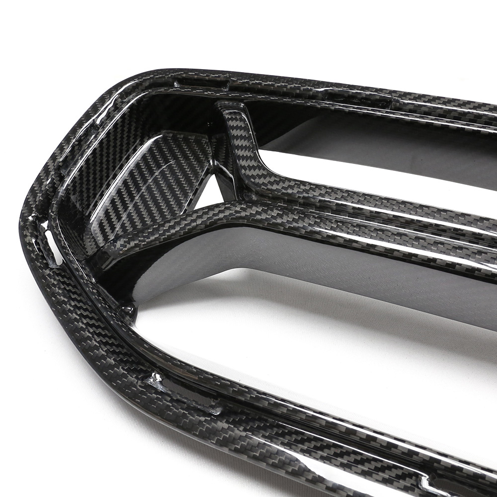 A carbon fiber car grille with a glossy finish, featuring an intricate weave pattern, rests on a plain white surface.