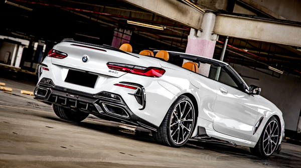 A white convertible sports car, displaying sleek design and chrome wheels, is parked in a dimly lit indoor structure. "BMW" badge and "840i" insignia visible on the rear.