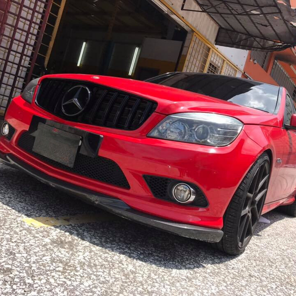 A red Mercedes-Benz car, parked with sleek, black wheels, sits in front of a building with an open garage door. The environment includes a textured pavement and nearby structures.
