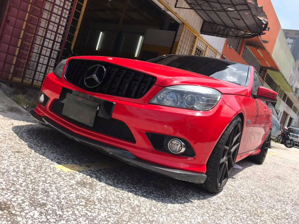 A red Mercedes-Benz car, parked with sleek, black wheels, sits in front of a building with an open garage door. The environment includes a textured pavement and nearby structures.