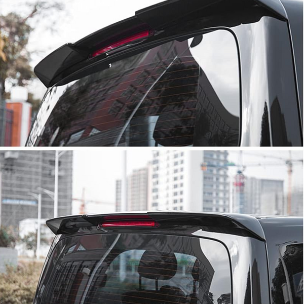 A black car rear spoiler with an integrated red brake light, attached above the rear window. The car is parked outdoors in a city area with buildings in the background.