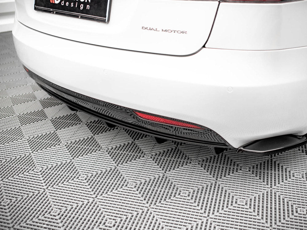 A white car's rear, labeled "DUAL MOTOR," is parked on a gray, textured floor. A red reflector is visible on the lower bumper, and the license plate includes "design."