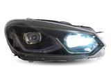 A car headlight is illuminated, emitting bright white light. The headlight features sleek, modern design lines with visible internal components, highlighted against a plain white background.