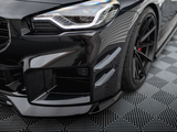 A sleek, black sports car shows its front headlight and grille, with a sporty bumper and aerodynamic features. It's parked on a textured, patterned surface, enhancing its modern appearance.