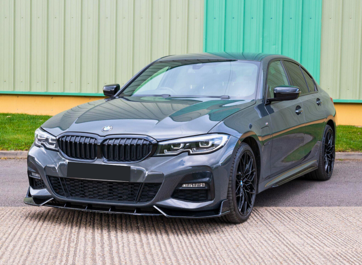 A sleek, dark-colored car is parked on a concrete surface with a green industrial building in the background. The car features distinctive black wheels and a prominent front grille.