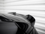 A sleek, black car spoiler is shown from a low angle; the surface reflects light. The background is a blurred, white, horizontal-striped wall.