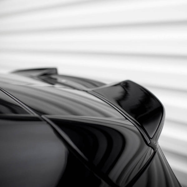 A sleek, black car spoiler is shown from a low angle; the surface reflects light. The background is a blurred, white, horizontal-striped wall.