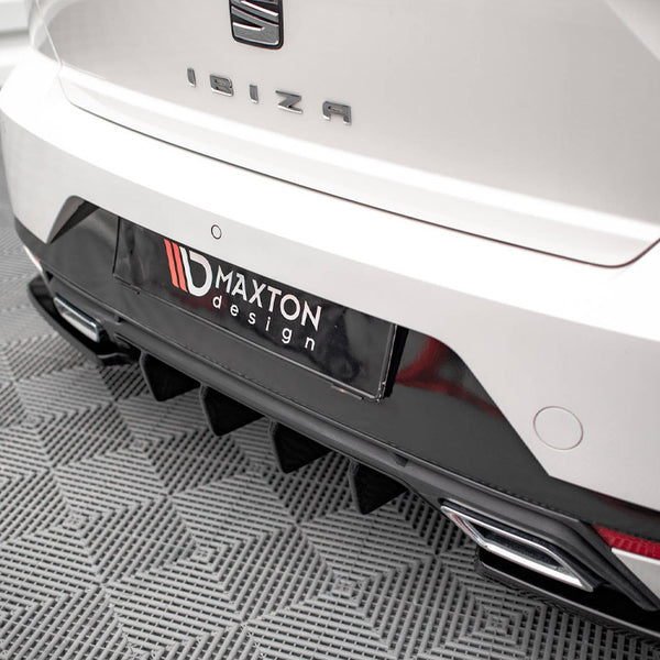 The rear of a white car with the word "IBIZA" and a "MAXTON design" label is parked on a patterned floor, featuring dual exhausts and a textured diffuser.