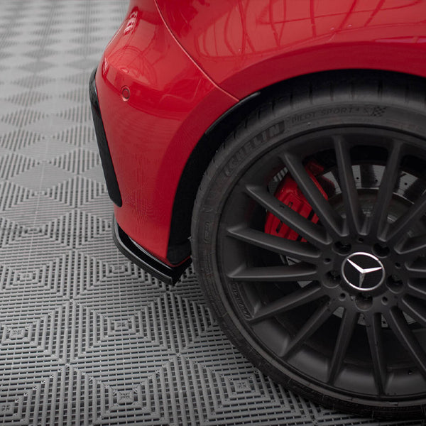 A black alloy wheel with a Mercedes logo is stationary on a patterned gray surface. The car, painted red, is partially visible with a rear fender.