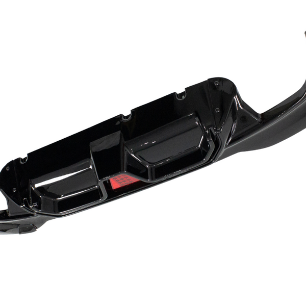 A glossy black car bumper with angular cutouts is isolated on a white background, featuring a central red reflective element.