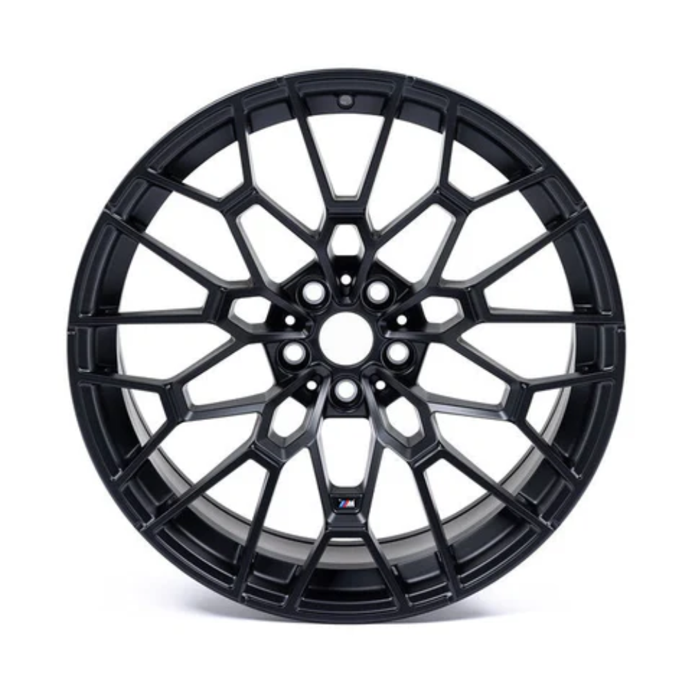 A black, intricately designed alloy wheel with a multi-spoke pattern, positioned upright on a plain white background, displaying an "M" logo near the hub.