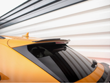 A yellow car's rear, featuring a tinted back window and a roof spoiler, is parked in front of a modern, striped wall in shades of white and black.