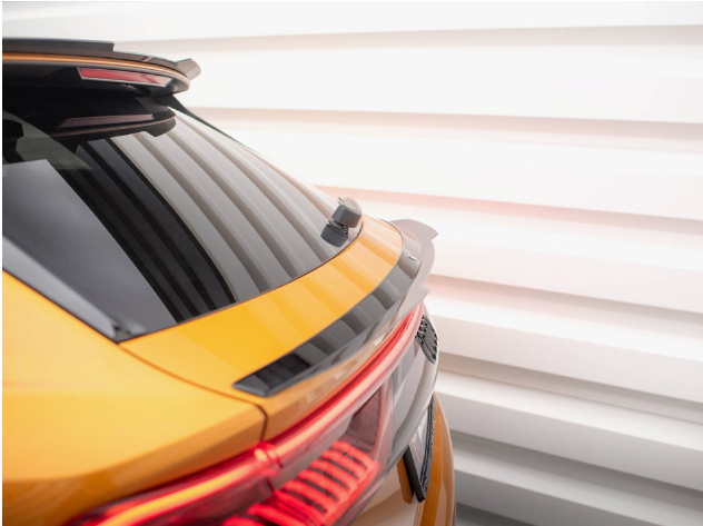 A gold car shows its rear with tinted windows, a small spoiler, and visible taillights in front of a bright, ribbed, white wall.