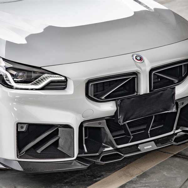 A sleek, white sports car stands in a garage. The car features a prominent grille, detailed headlights, and a carbon fiber front bumper. The tire reads "Pirelli".