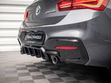 A grey BMW M240i is parked on a checkered floor indoors. It features a visible rear bumper with dual exhausts. The license plate reads 