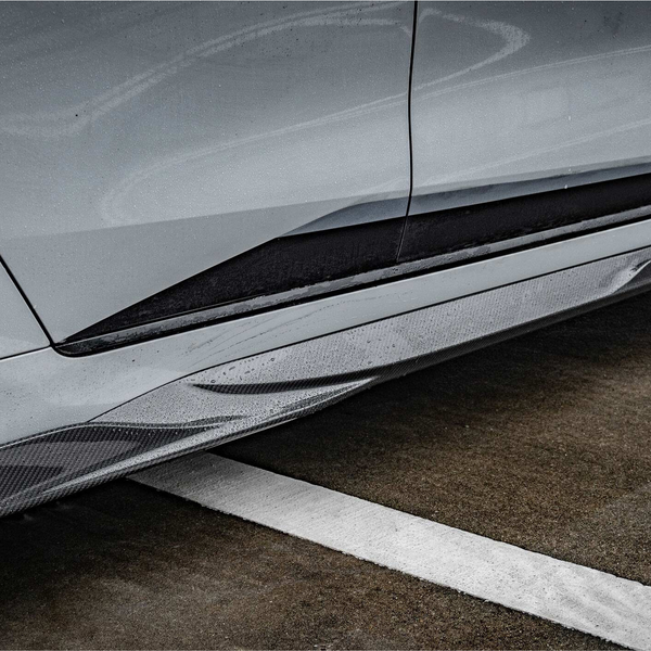Car side skirt with "M PERFORMANCE" text is enhanced by raindrops. It's part of a sleek vehicle parked on wet pavement with a white painted line.