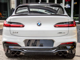 A white BMW X4 car is parked, displaying its rear view with distinctive taillights and dual exhaust pipes; it's positioned in an urban environment near a building entrance.