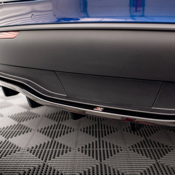 A blue car's rear bumper features a sleek aerodynamic design with a diffuser. A small "ADRO" logo is visible. The car is on a checkered pattern floor, likely in a showroom.
