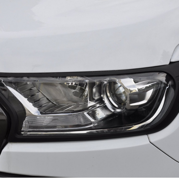 A close-up view of a car headlight, featuring a sleek, angular design with reflective surfaces, set within a white vehicle body. The headlight is bordered by black trim.
