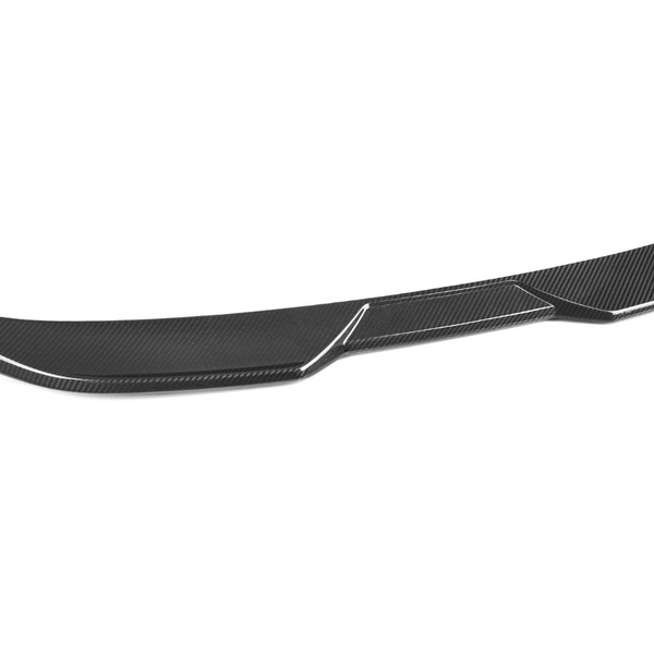 A carbon fiber car spoiler, curved and streamlined, lies against a plain white background, highlighting its smooth, aerodynamic design and textured surface.