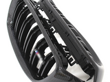 A black carbon fiber car grille with multiple vertical slats lies against a white background, displaying its glossy finish and intricate design details.