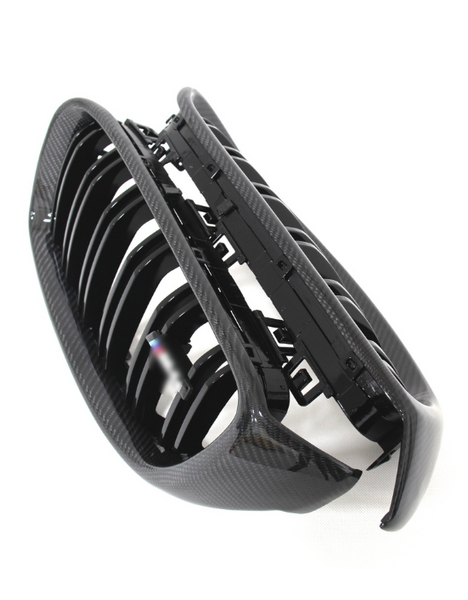 A black carbon fiber car grille with multiple vertical slats lies against a white background, displaying its glossy finish and intricate design details.