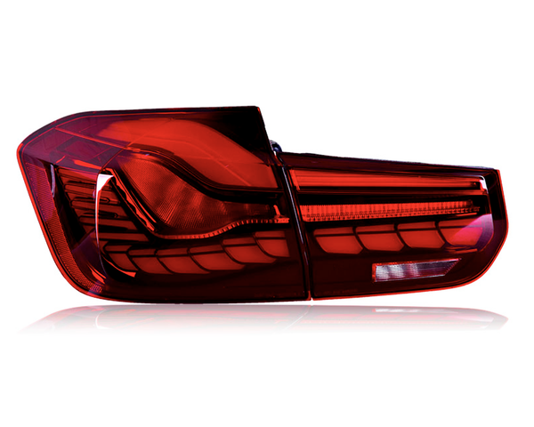 A car taillight is illuminated brightly, featuring a red and intricate design. The taillight is isolated against a plain white background, highlighting its sleek and modern curves.