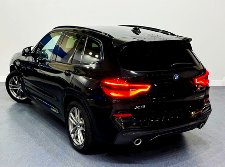 A black SUV with glowing red tail lights is stationary in a showroom, featuring "X3" and "xDrive30d" logos on the rear.