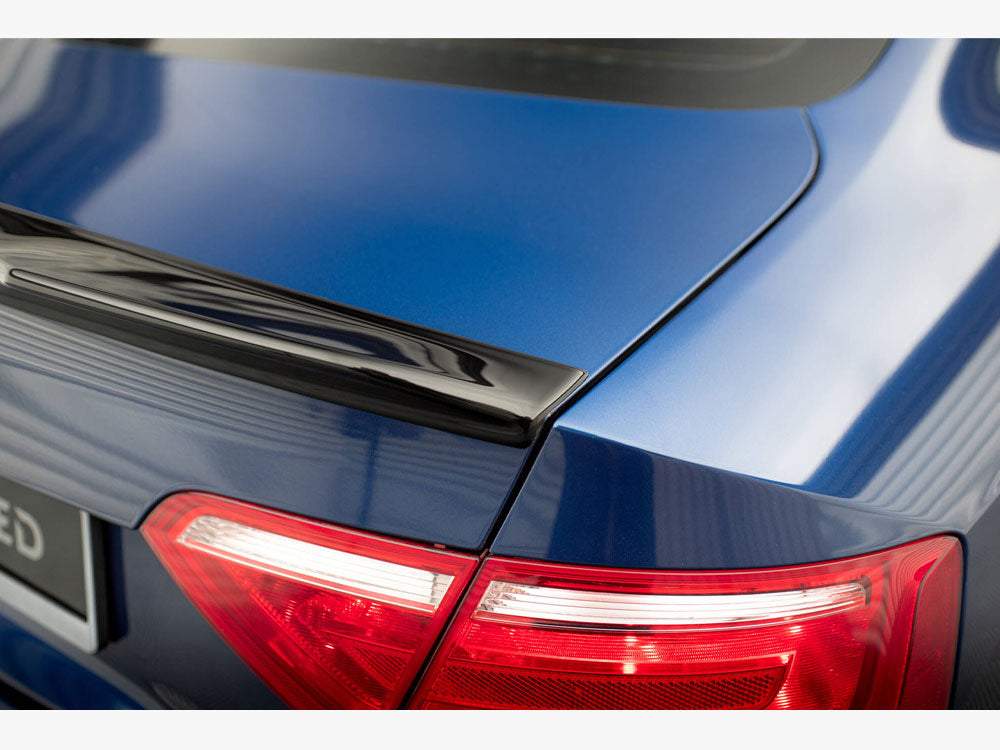 Car rear section features a blue trunk with a black spoiler, and illuminated red tail lights. Partial license plate text reads "ED." The car is parked indoors.