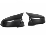 Two black carbon fiber car side mirror covers are positioned against a plain white background, showcasing their glossy, textured surface and sleek, aerodynamic shape.