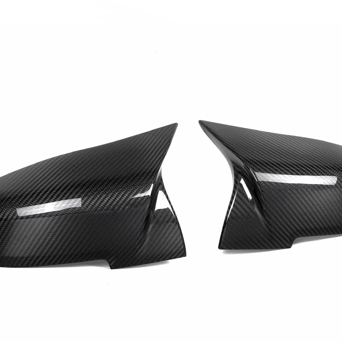 Two carbon fiber mirror covers are positioned side by side, facing each other against a plain white background, reflecting light subtly across their glossy, textured surfaces.