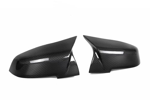Two sleek carbon fiber side mirror covers are positioned facing each other against a plain white background. The glossy texture highlights their aerodynamic design.