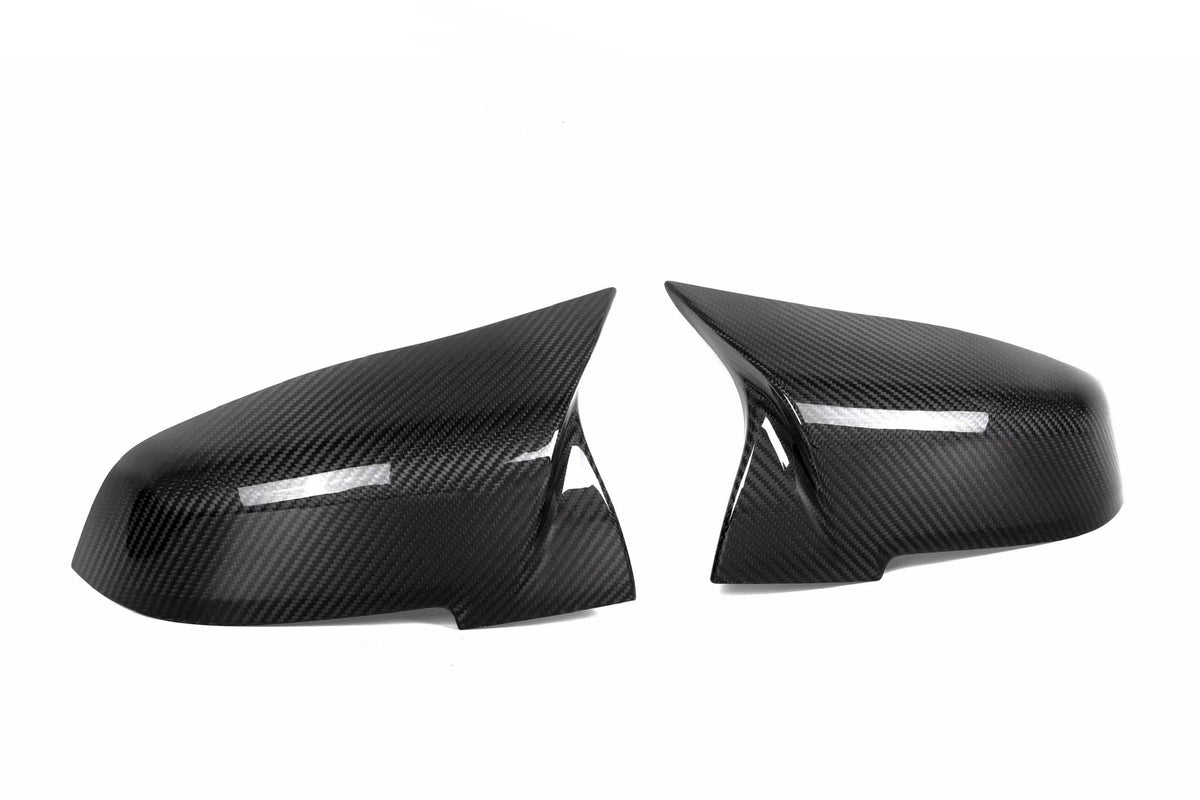 Two carbon fiber car mirror covers, resting side by side on a white background, showcasing their glossy texture and aerodynamic design.