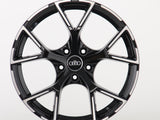 A glossy black car rim features five angular spokes and the Audi logo in the center, resting against a plain white background.