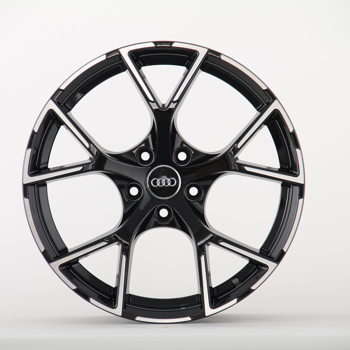 A glossy black car rim features five angular spokes and the Audi logo in the center, resting against a plain white background.