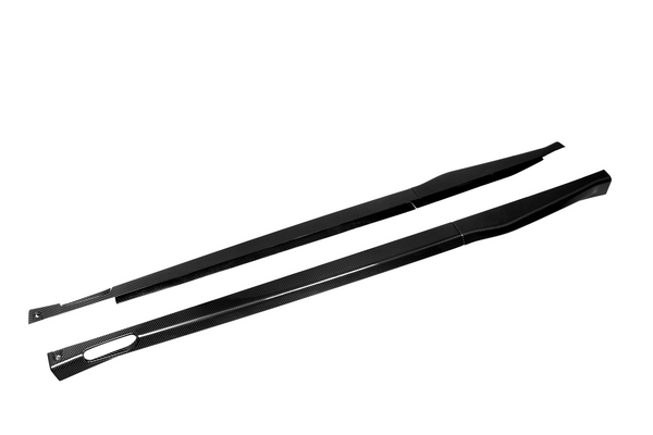 Two black carbon-fiber side skirts lie parallel, showcasing sleek design and aerodynamic shape against a plain white background.