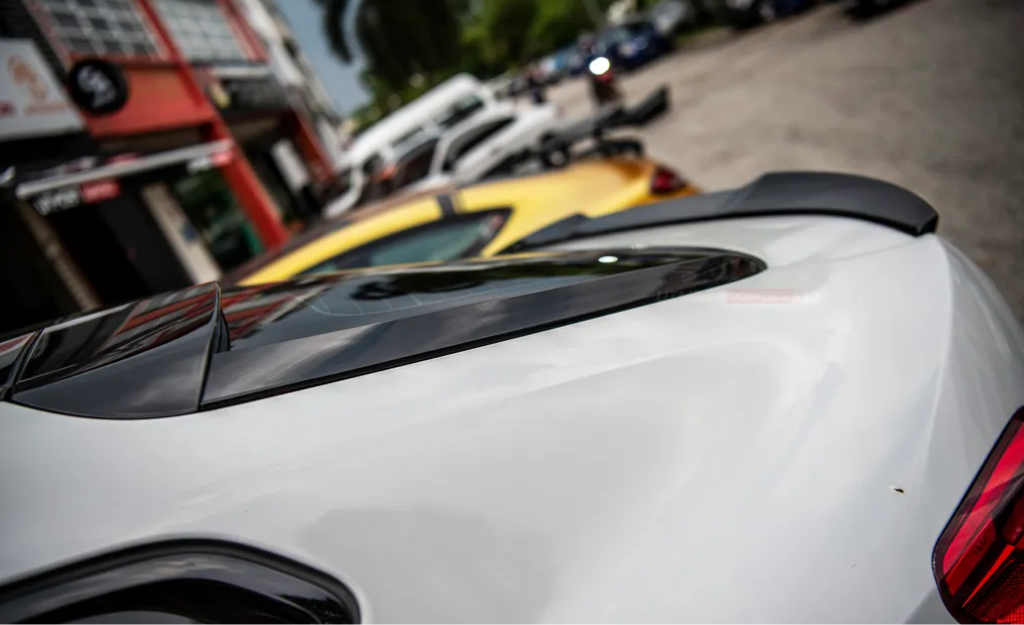 White car with a black roof detail, parked on a street alongside a yellow car. Background includes storefronts and additional parked vehicles.