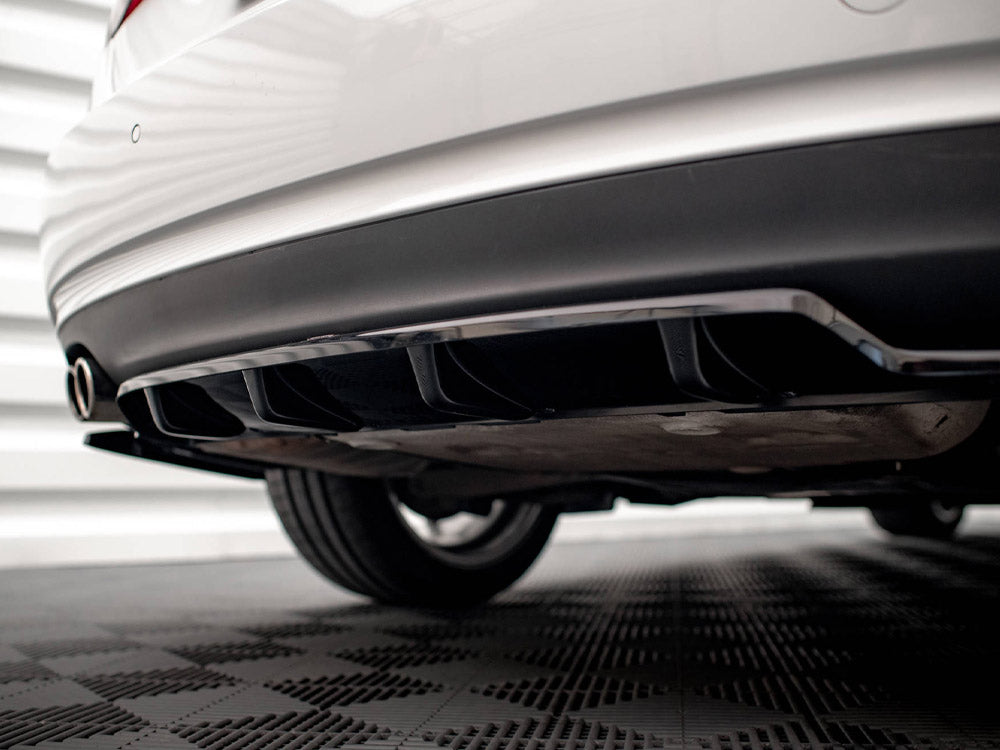 The rear of a white car with a black diffuser and dual exhaust pipes is parked on a checkered floor, against a backdrop of horizontal white panels.