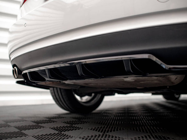 The rear of a white car with a black diffuser and dual exhaust pipes is parked on a checkered floor, against a backdrop of horizontal white panels.