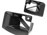 Carbon fiber air vents with a glossy finish are shown. One is angled upward and the other aligns horizontally. The white background highlights the sleek, geometric design.